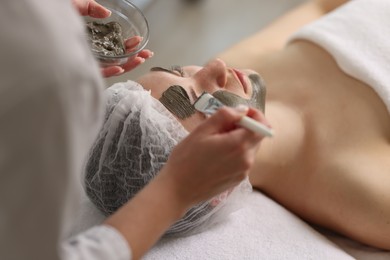 Cosmetologist applying mask on woman's face, closeup