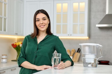 Photo of Woman with glass of water and filter jug in kitchen