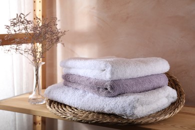 Photo of Stacked soft towels and flowers on wooden shelf indoors