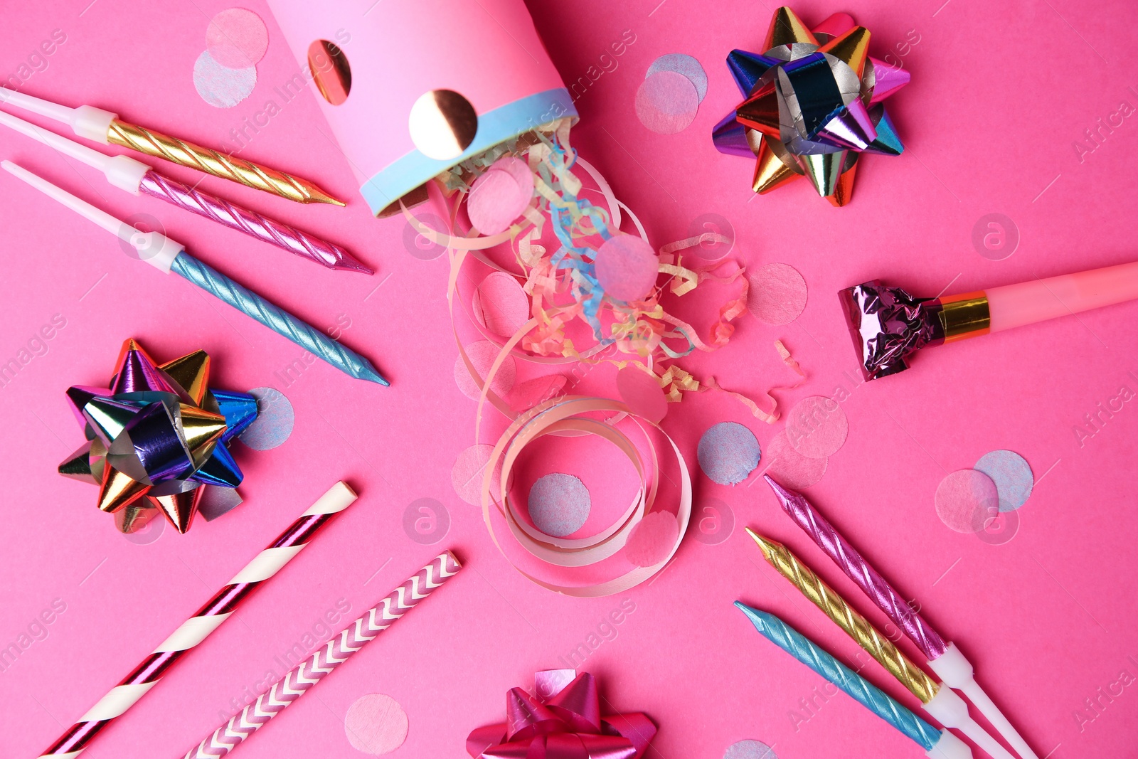 Photo of Party cracker and different festive items on bright pink background, flat lay