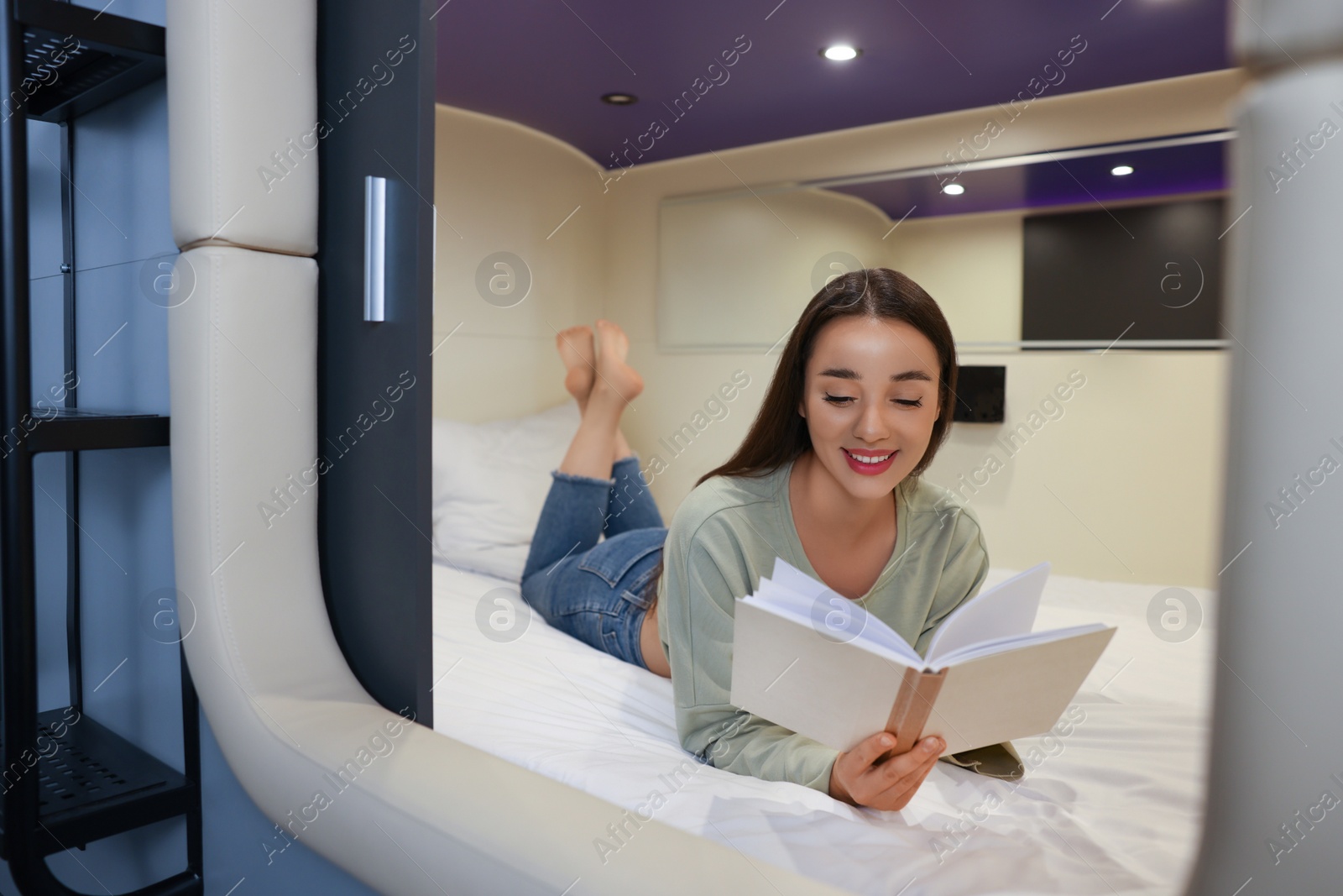 Photo of Happy young woman reading book in capsule of pod hostel