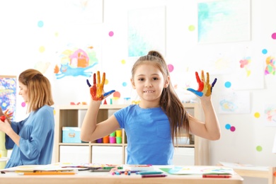 Photo of Cute little child showing painted hands at lesson indoors