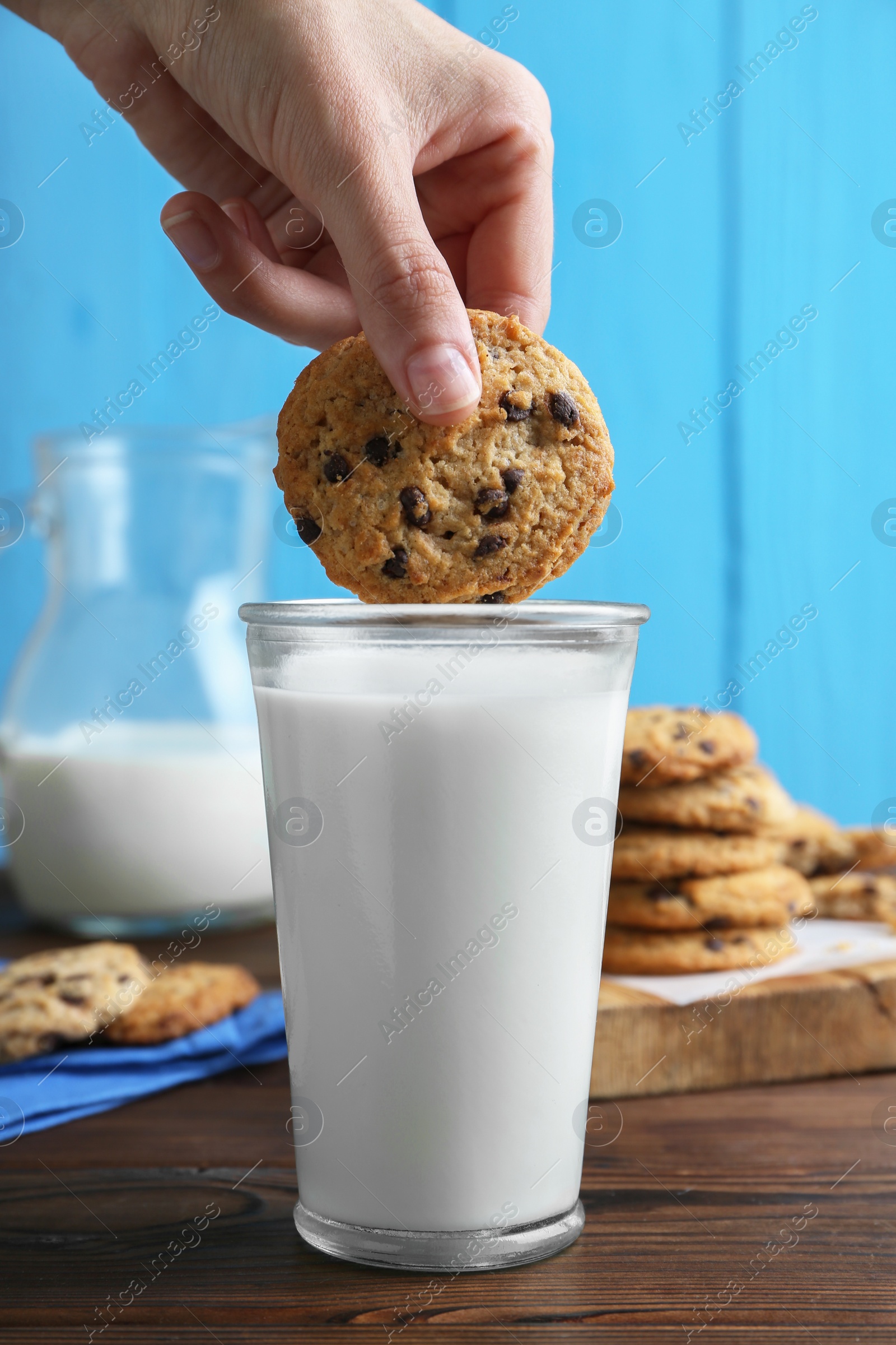 Woman dipping delicious chocolate chip cookie into glass of milk at wooden table, closeup Photo of Woman dipping delicious chocolate chip cookie into glass of milk at wooden table, closeup
