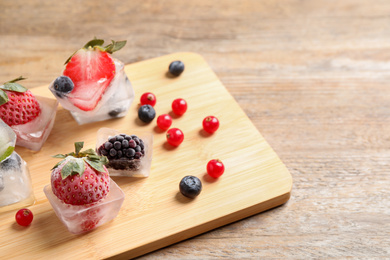 Photo of Ice cubes with different berries and mint on wooden table