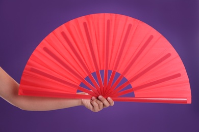 Woman holding red hand fan on purple background, closeup