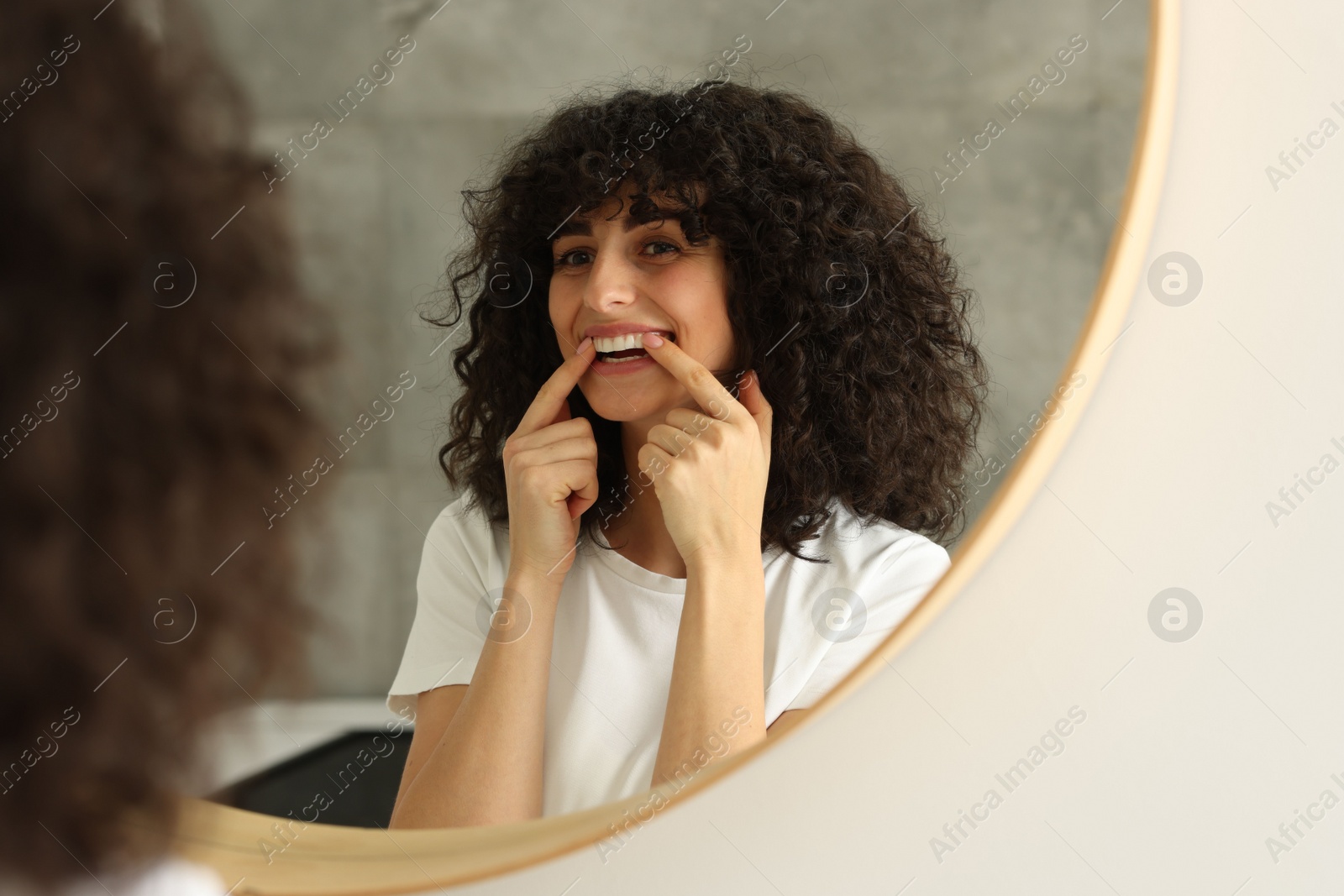 Photo of Young woman applying whitening strip on her teeth indoors