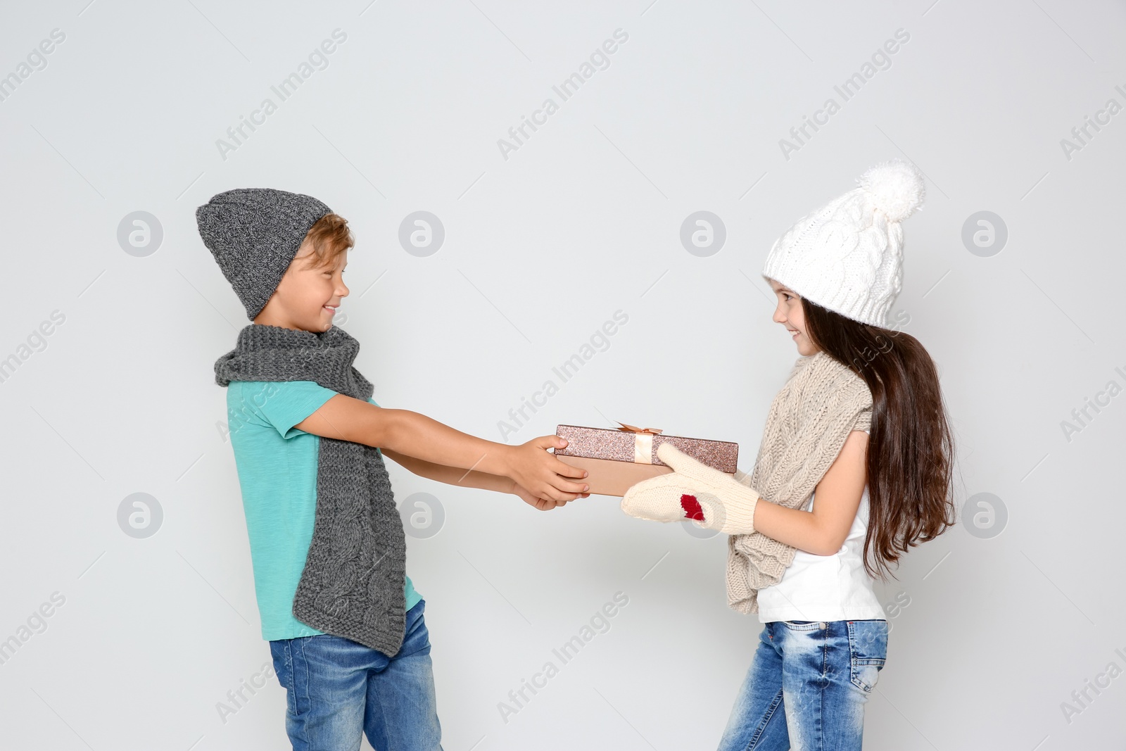 Photo of Cute little children in warm clothes with Christmas gift box on light background