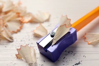Photo of Violet sharpener with pencil shavings on white wooden table, closeup