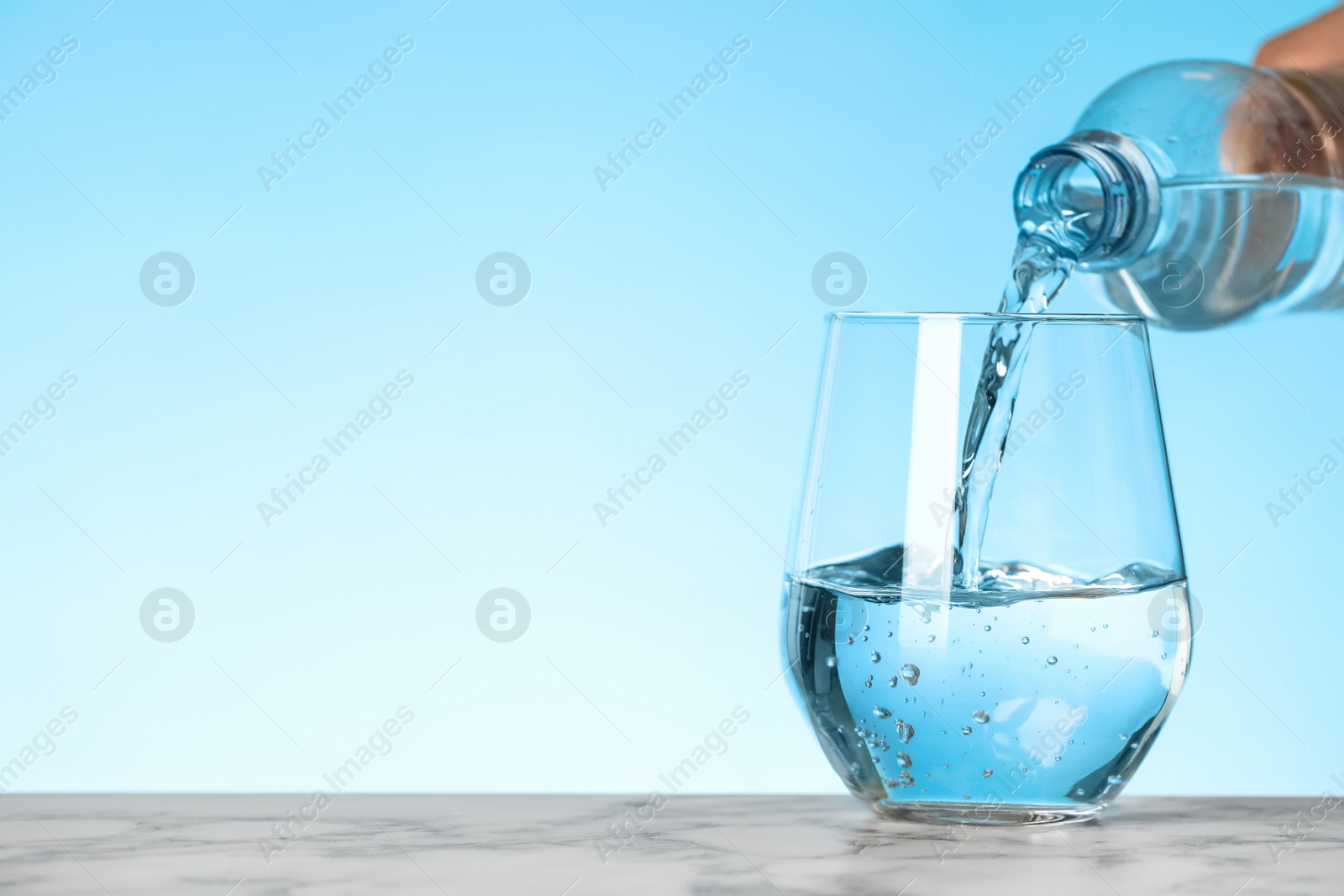 Photo of Pouring water from bottle into glass on blue background, space for text. Refreshing drink