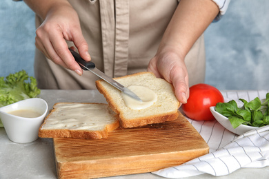 Photo of Woman spreading sauce on sandwich at light grey marble table, closeup