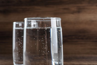 Photo of Glasses of soda water on wooden background, closeup. Space for text