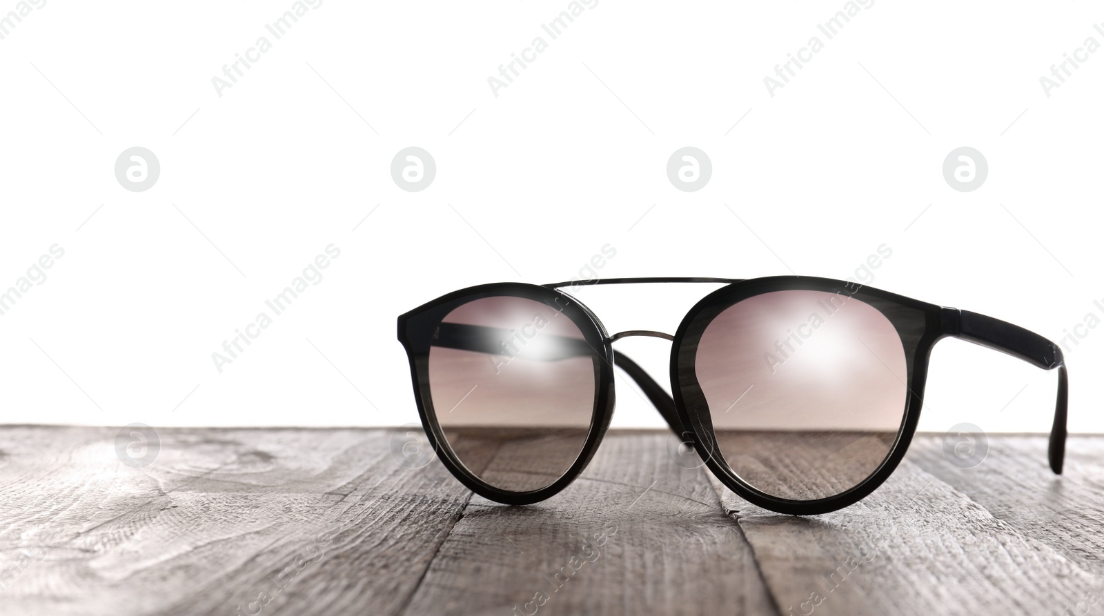 Photo of Stylish sunglasses on wooden table against white background