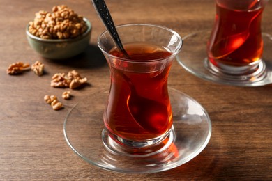 Photo of Glasses of traditional Turkish tea and walnuts on wooden table, closeup