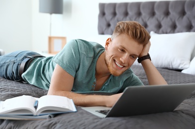 Photo of Young man using laptop while lying on bed at home