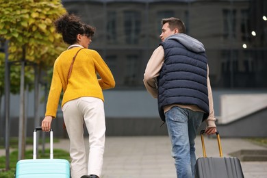 Photo of Being late. Worried couple with suitcases running outdoors, back view