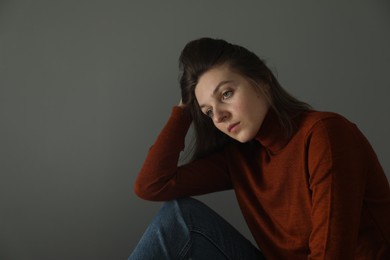 Sad young woman near grey wall indoors, space for text