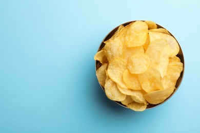 Delicious crispy potato chips in bowl on color background, top view with space for text