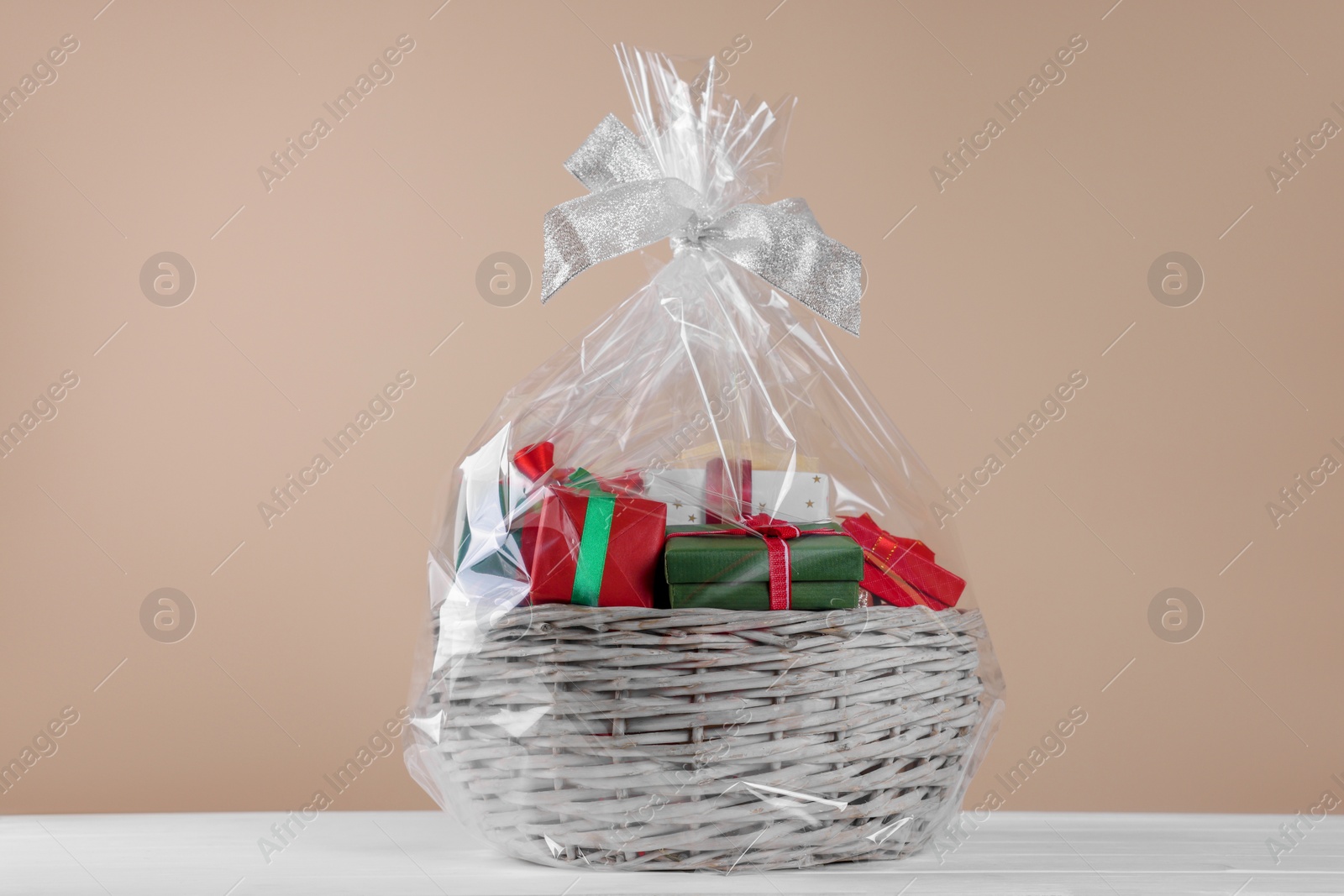 Photo of Wicker basket full of gift boxes on white wooden table against beige background