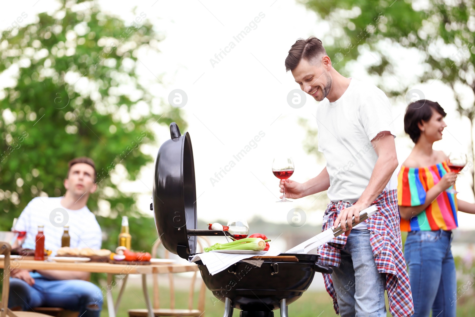 Photo of Young people having barbecue with modern grill outdoors