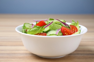 Bowl of tasty salad with cucumber, tomato and lettuce on table