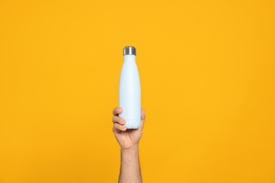 Man holding thermo bottle on orange background, closeup