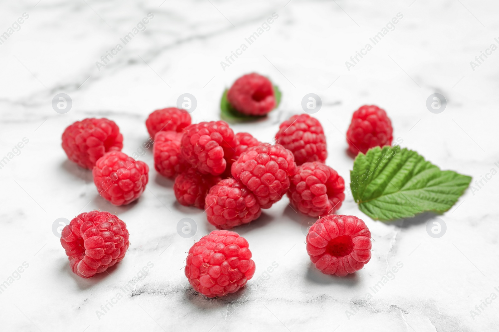 Photo of Ripe aromatic raspberries on marble table, closeup