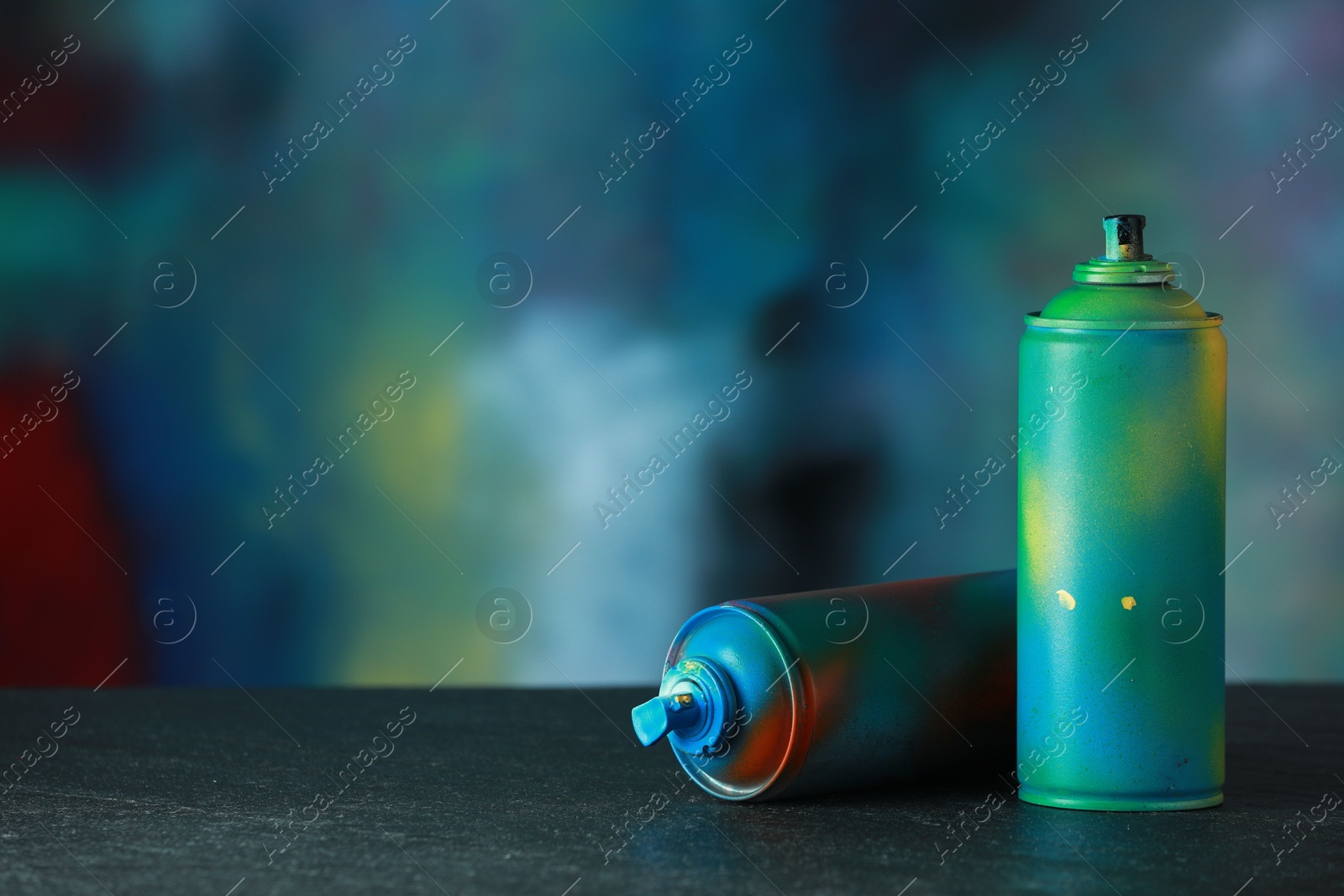 Photo of Two spray paint cans on gray surface against color background, space for text