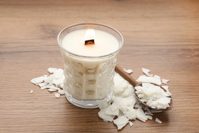 Burning soy candle, wax flakes and spoon on wooden table