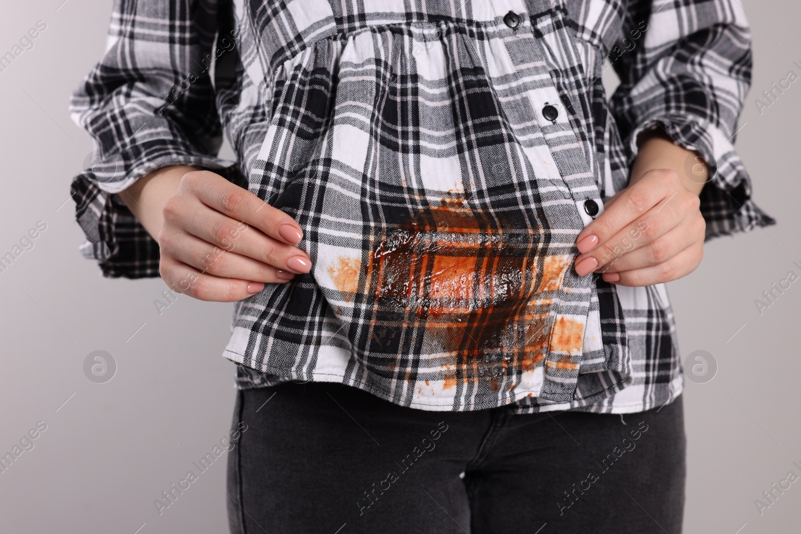 Photo of Woman showing stain from sauce on her shirt against light grey background, closeup