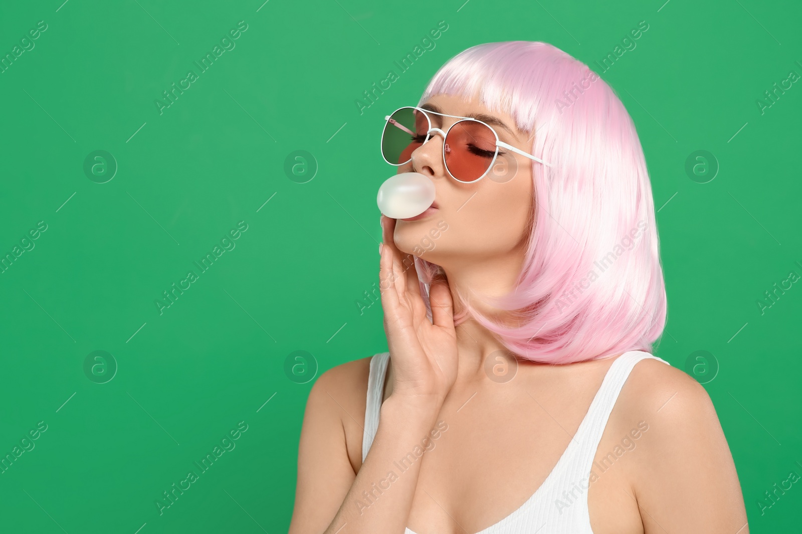 Photo of Beautiful woman in sunglasses blowing bubble gum on green background, space for text