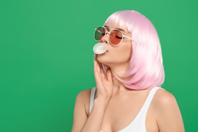 Beautiful woman in sunglasses blowing bubble gum on green background, space for text