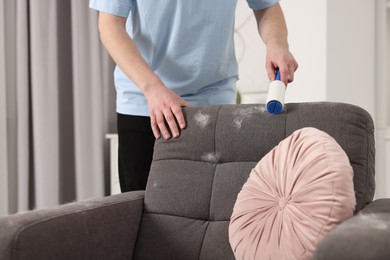 Photo of Pet shedding. Man with lint roller removing dog's hair from armchair at home, closeup