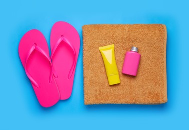 Photo of Sunscreens, flip flops and towel on light blue background, flat lay