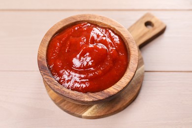 Photo of Delicious ketchup in bowl on light wooden table, closeup. Tomato sauce