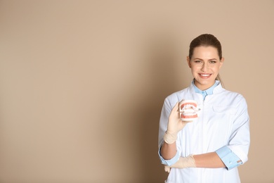 Photo of Female dentist holding jaws model on color background. Space for text