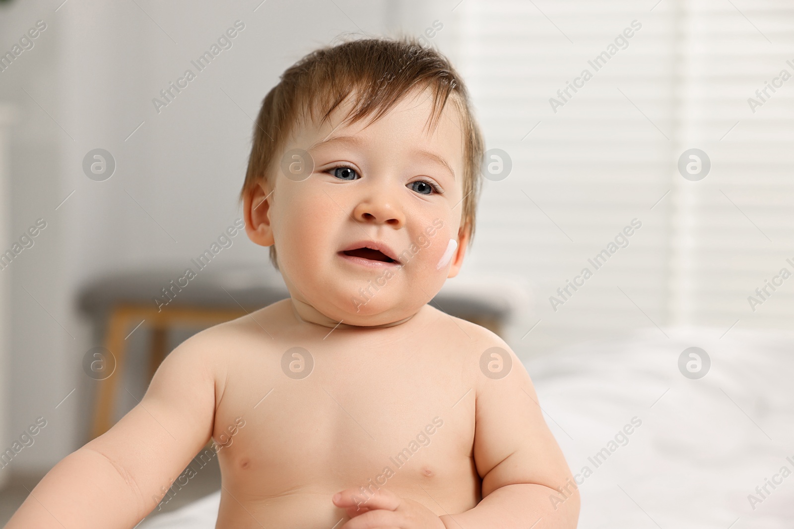 Photo of Cute little baby with moisturizing cream on face indoors