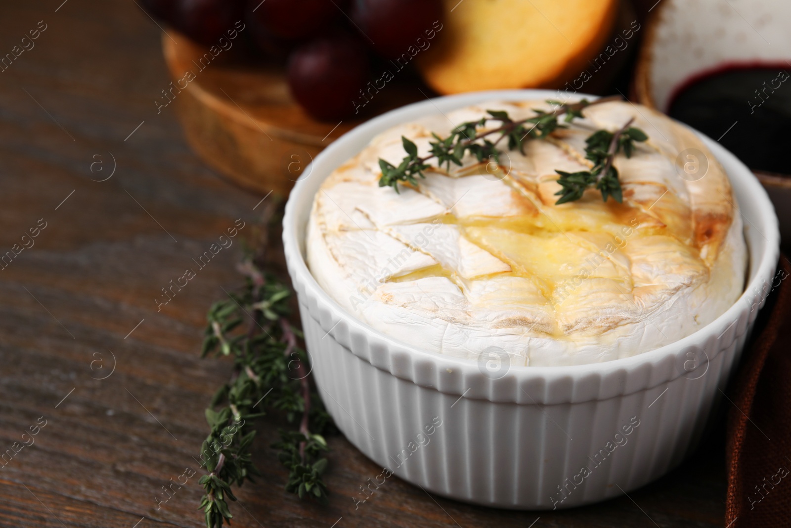 Photo of Tasty baked camembert and thyme in bowl on wooden table, closeup. Space for text