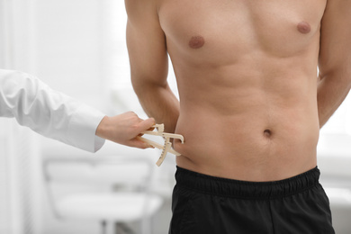 Photo of Nutritionist measuring man's body fat layer with caliper on blurred background, closeup