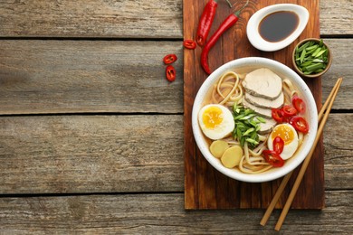 Photo of Delicious ramen in bowl served on wooden table, flat lay and space for text. Noodle soup