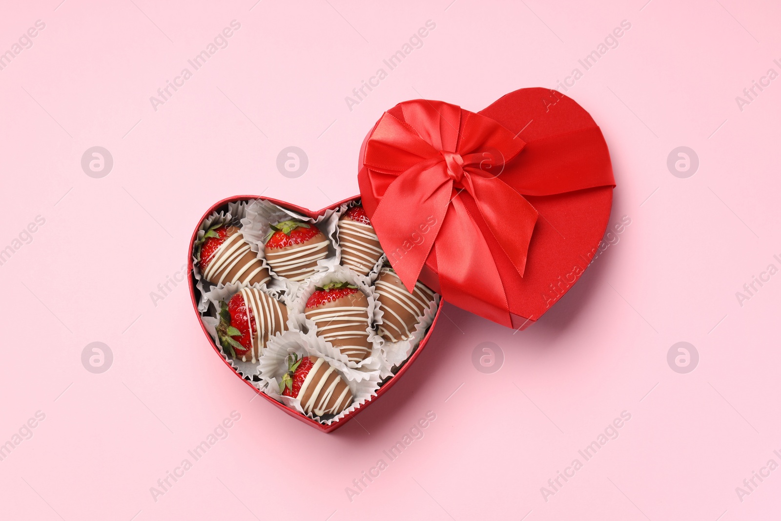 Photo of Heart shaped box with delicious chocolate covered strawberries on pink background, top view