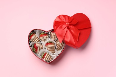 Photo of Heart shaped box with delicious chocolate covered strawberries on pink background, top view