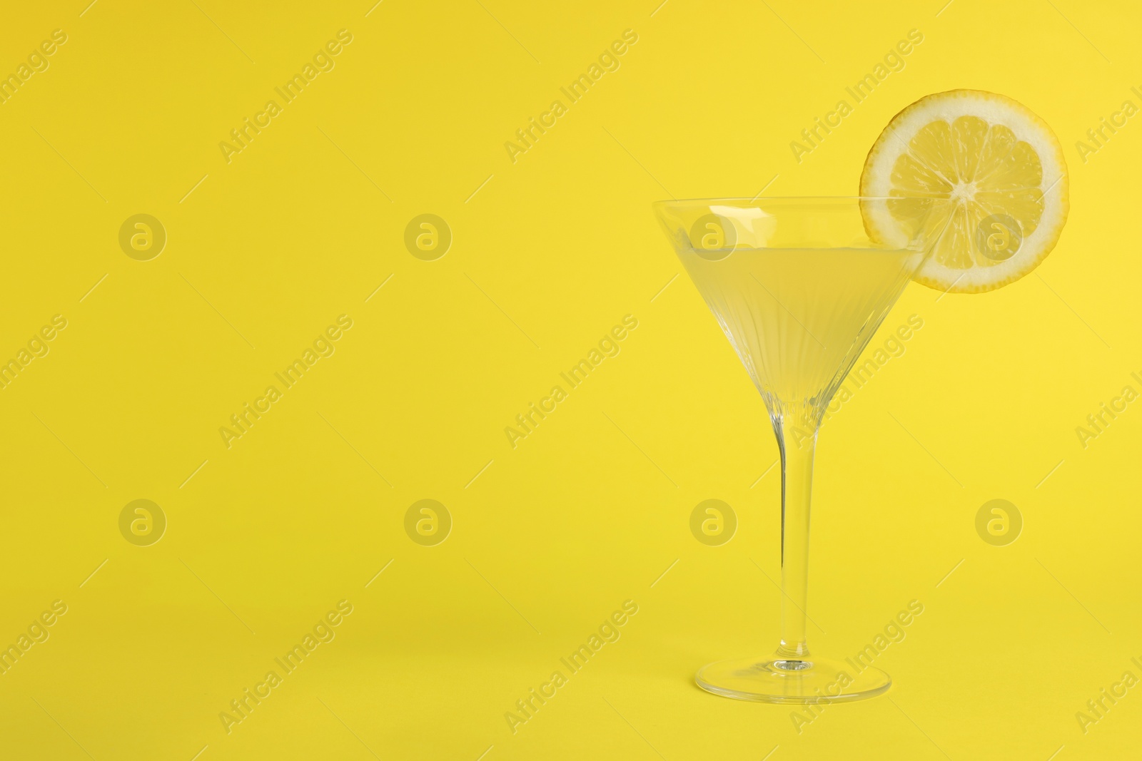 Photo of Martini glass of refreshing cocktail with lemon slice on yellow background, space for text