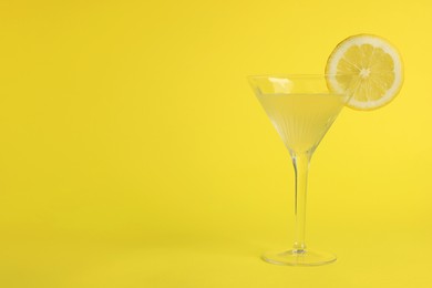 Photo of Martini glass of refreshing cocktail with lemon slice on yellow background, space for text