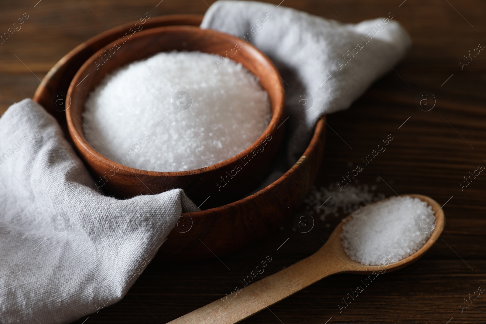 Photo of Organic salt in bowl and spoon on wooden table, closeup