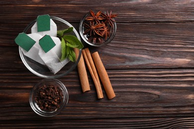 Photo of Tea bags and ingredients on wooden table, flat lay. Space for text
