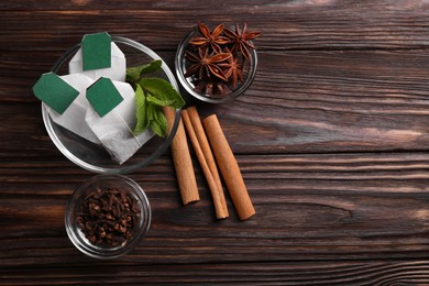 Tea bags and ingredients on wooden table, flat lay. Space for text