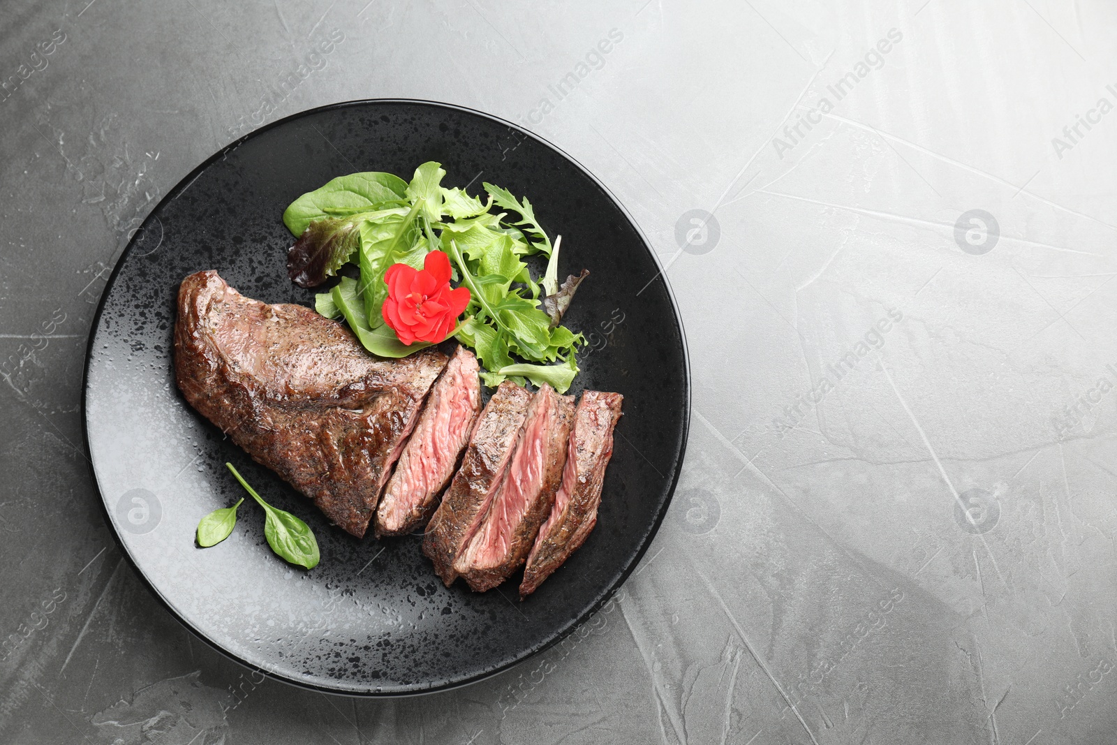 Photo of Pieces of delicious grilled beef meat and greens on grey table, top view. Space for text