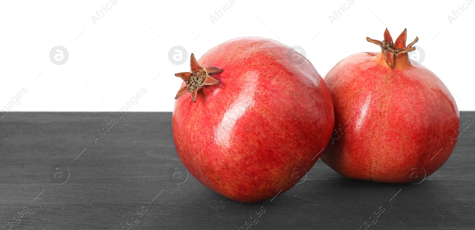 Photo of Fresh pomegranates on black wooden table against white background, space for text