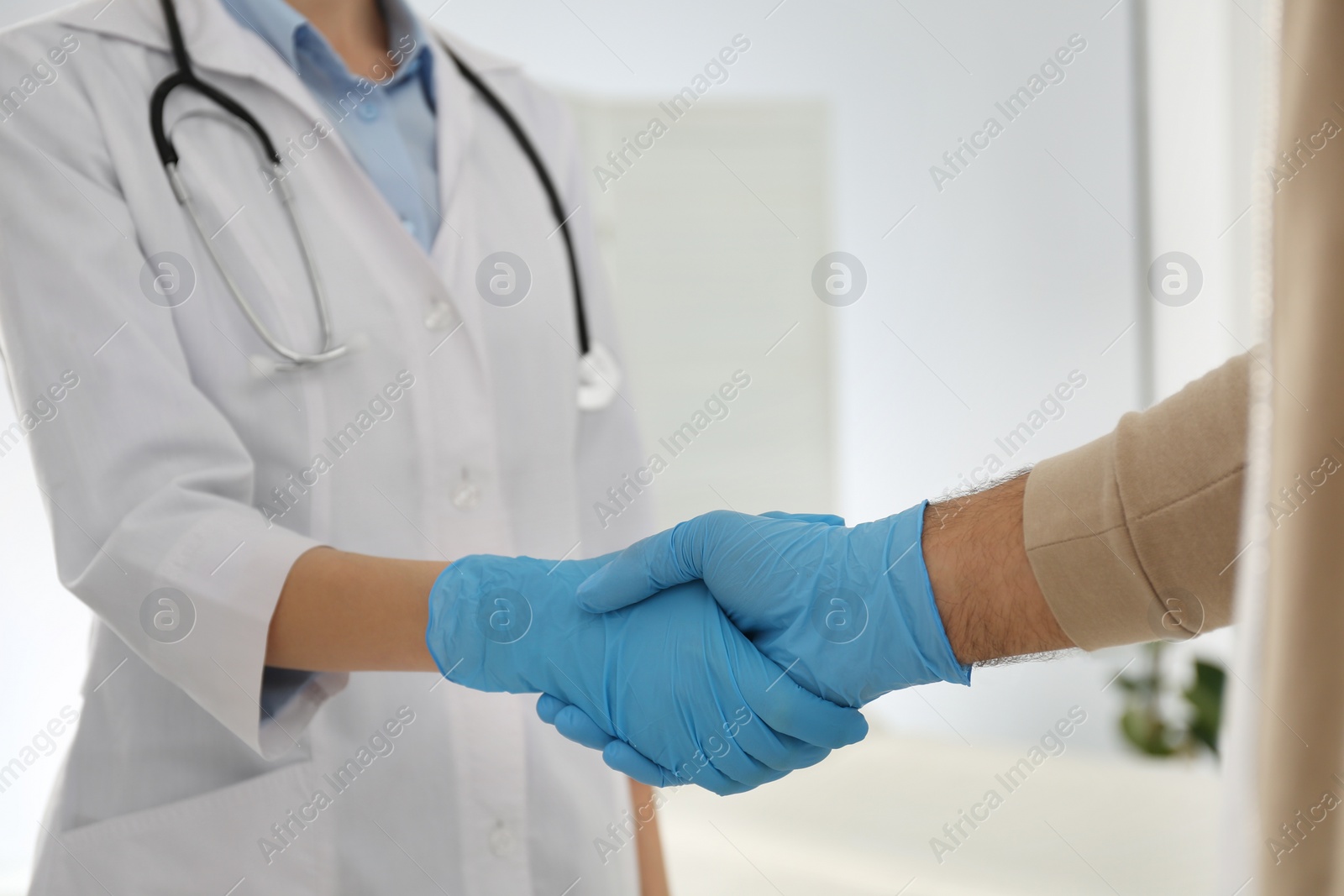 Photo of Doctor and patient in protective gloves shaking hands indoors, closeup