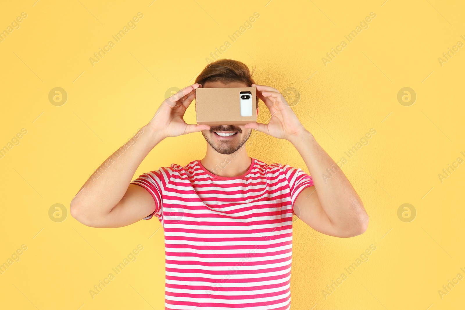 Photo of Young man using cardboard virtual reality headset on color background